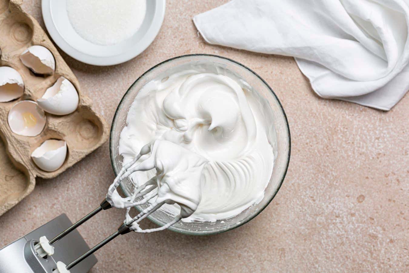 Beaten egg whites with sugar for Meringue in a mixing bowl with an electric hand whisk. Cooking process with kitchen utensils.