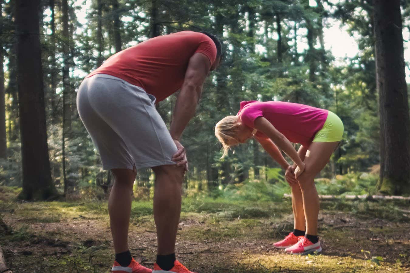 Exhausted Caucasian man and woman taking a break after running in the forest